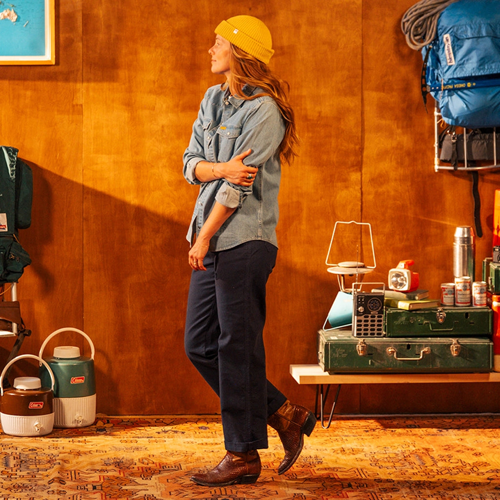 Person wearing a yellow beanie and blue shirt standing in a room with camping gear