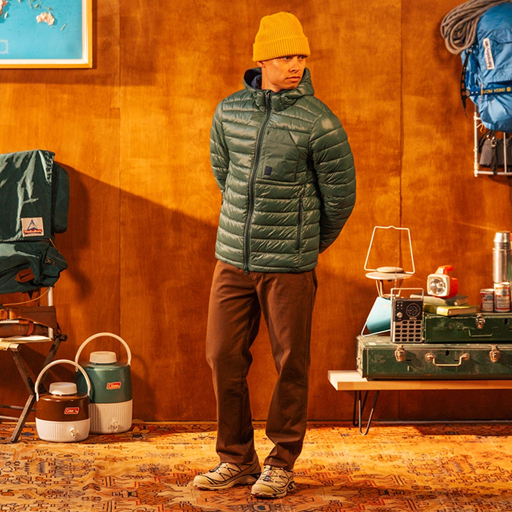 Person wearing a green puffer jacket and yellow beanie against an orange wall