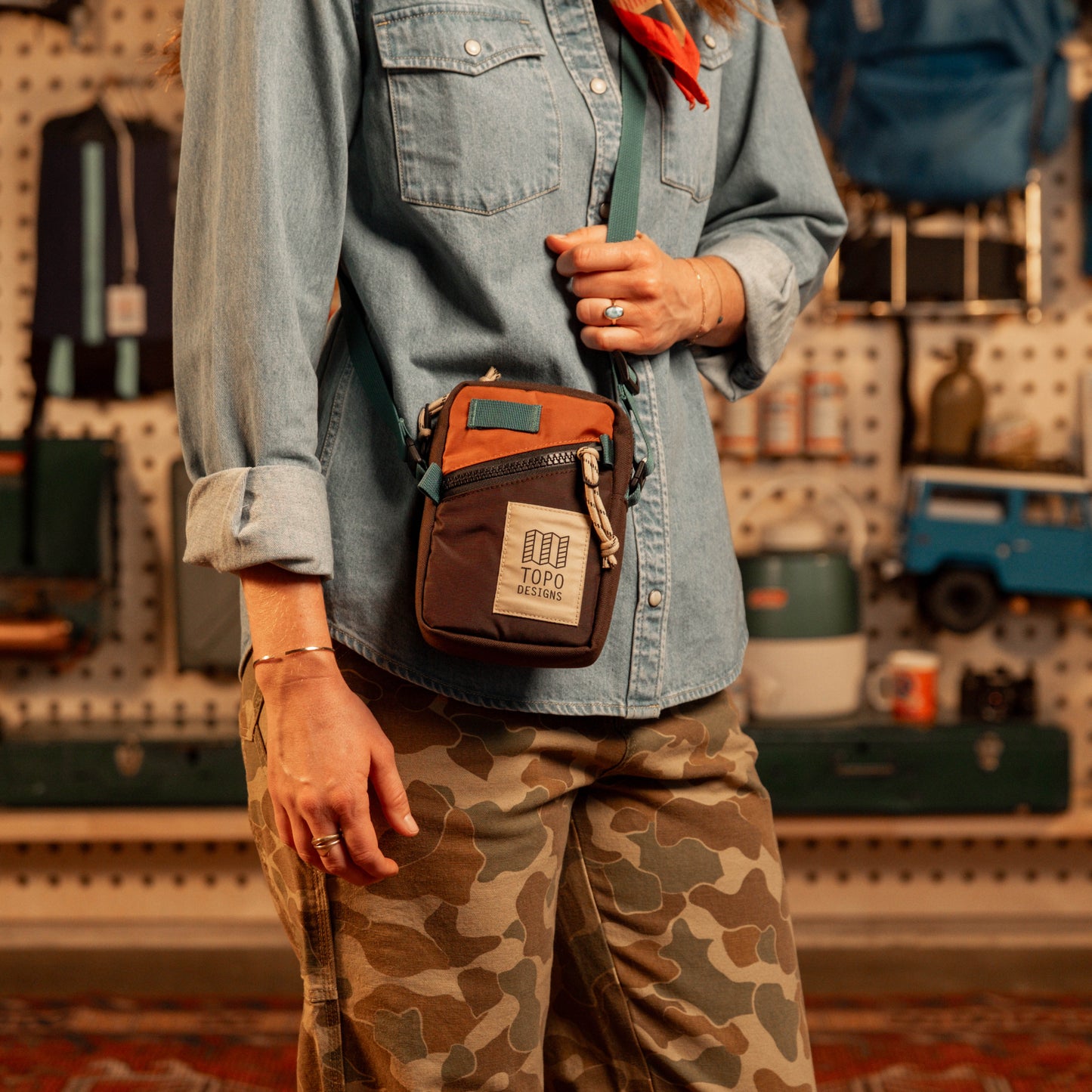 Person wearing a brown waist bag with 'Topo Designs' branding in a store setting.
