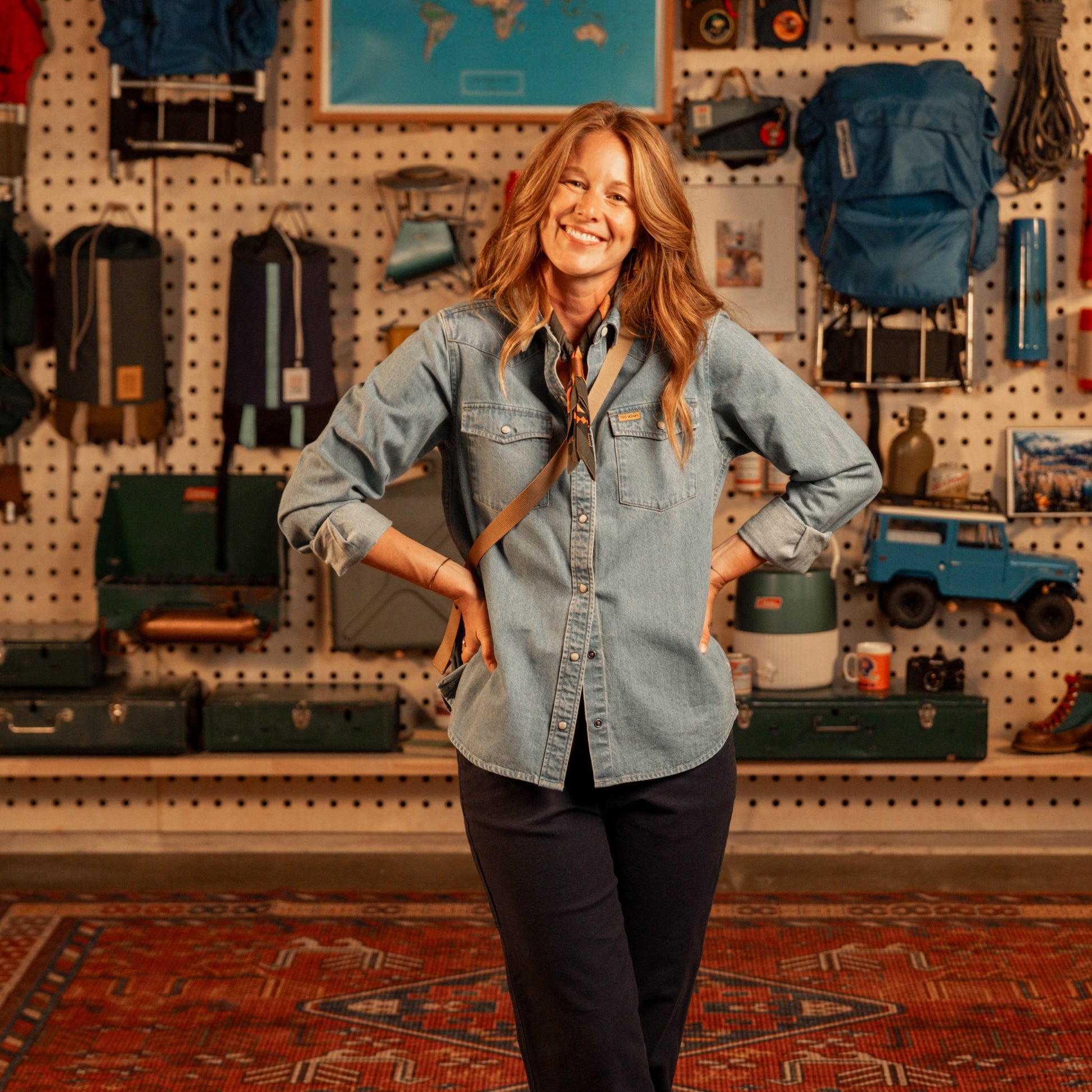 Woman in a "light denim" shirt standing in a store with various items on the wall behind her.