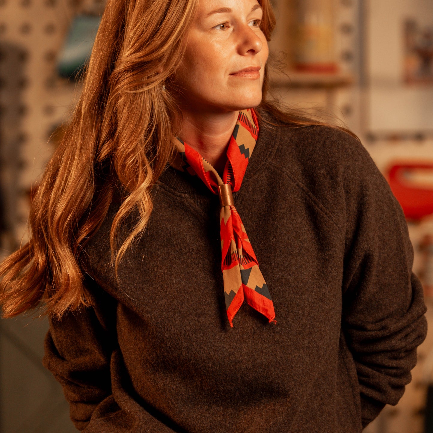 Woman wearing a brown sweater and red patterned scarf indoors