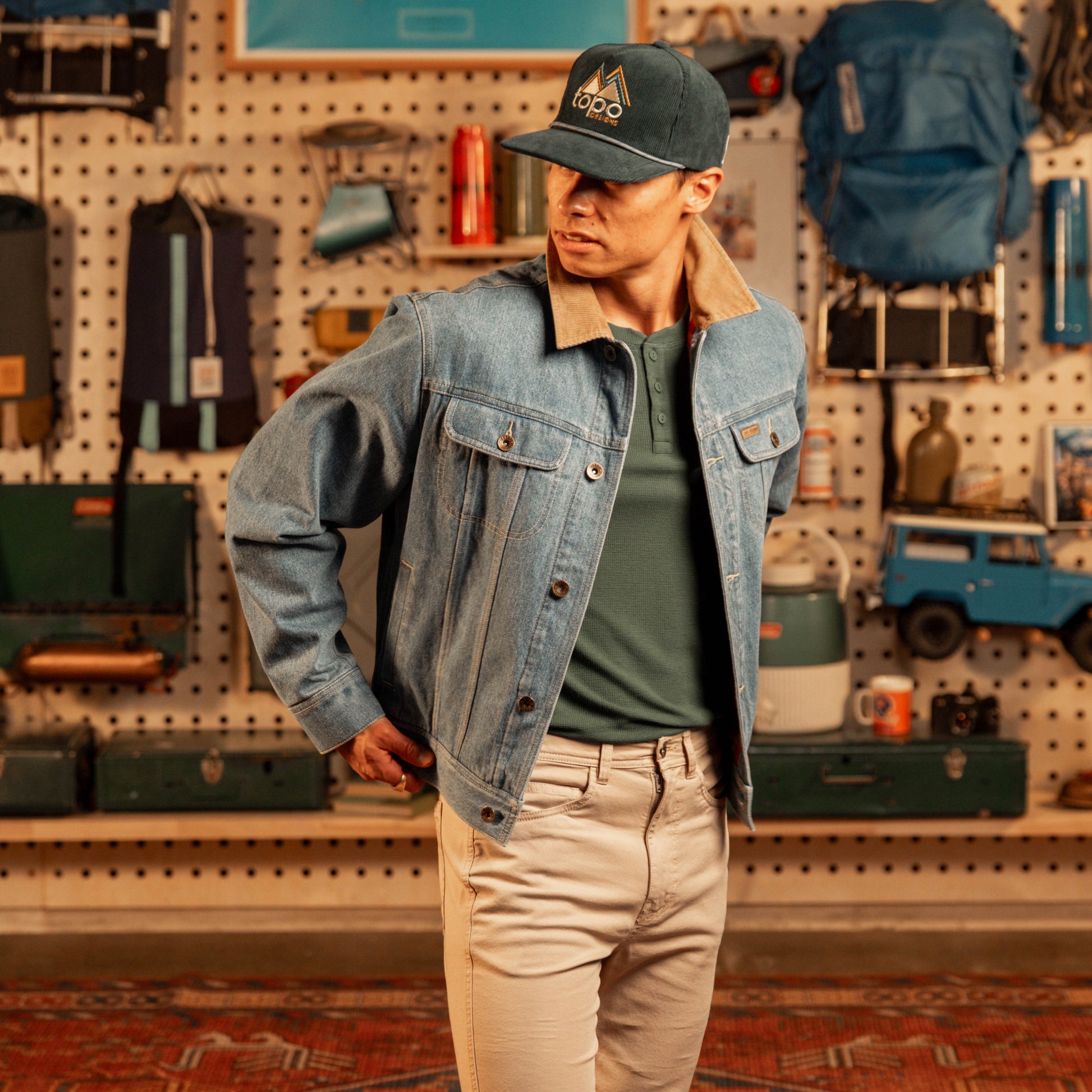 Person wearing a denim jacket and cap in a store setting with various items on shelves.