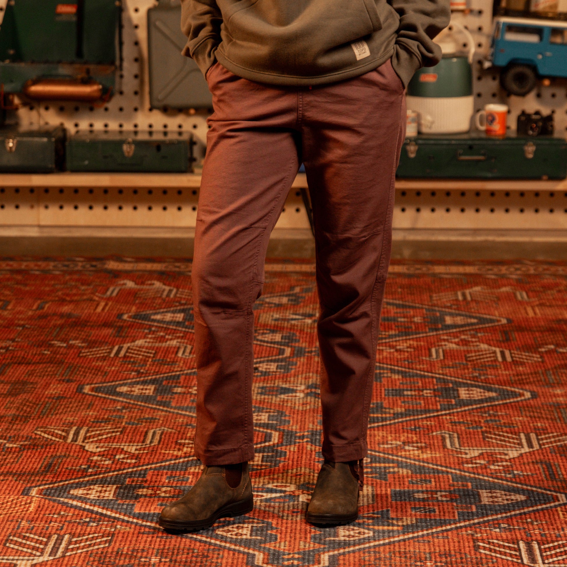 Person wearing brown pants standing on a patterned rug in a workshop setting