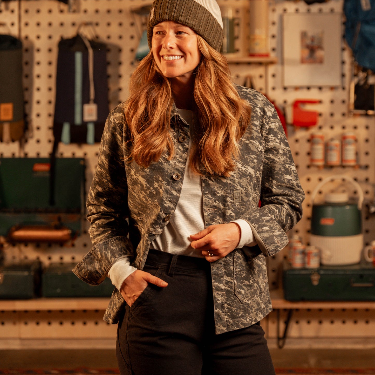 Woman wearing a camouflage jacket and beanie in a workshop setting