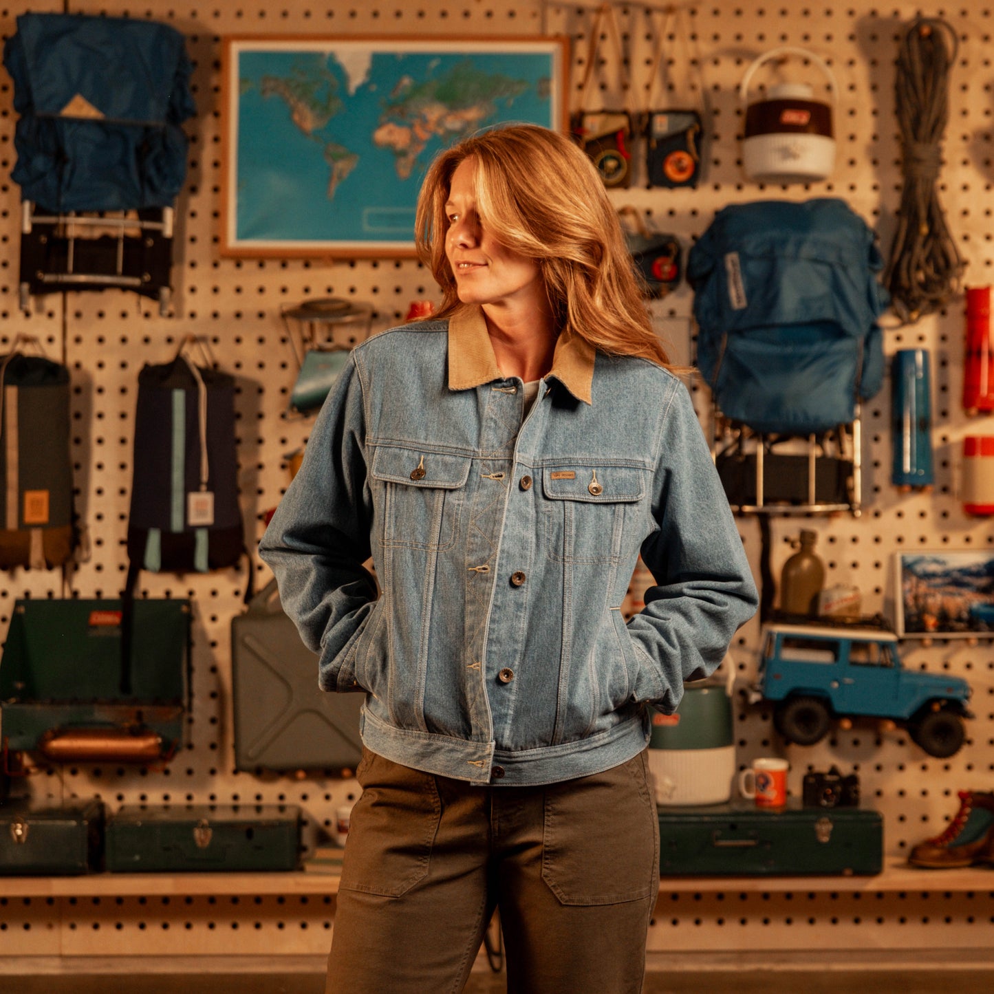 Woman wearing a denim jacket standing in a store with various items on the wall.