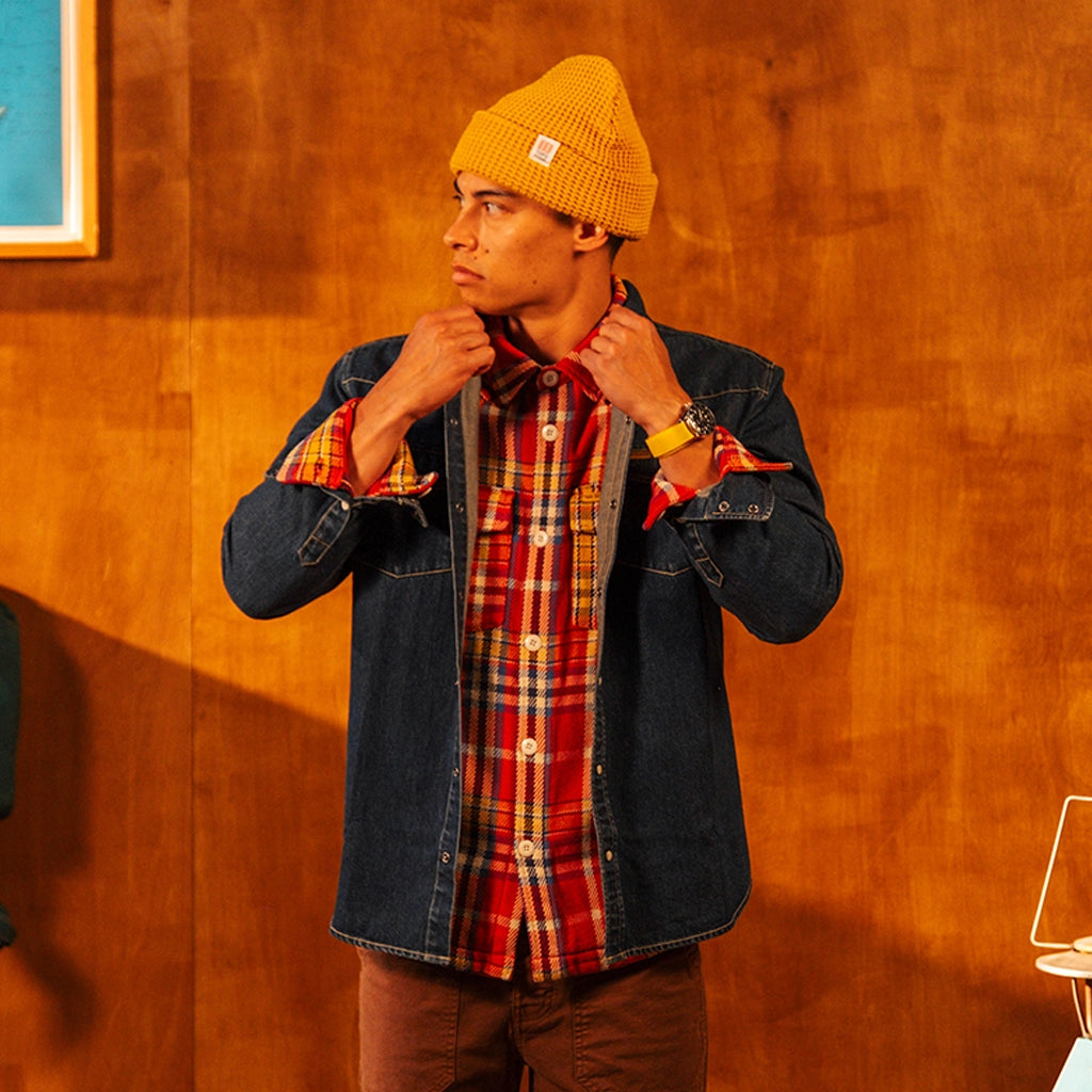 General image of person wearing a yellow waffle knit beanie standing against a white wall.