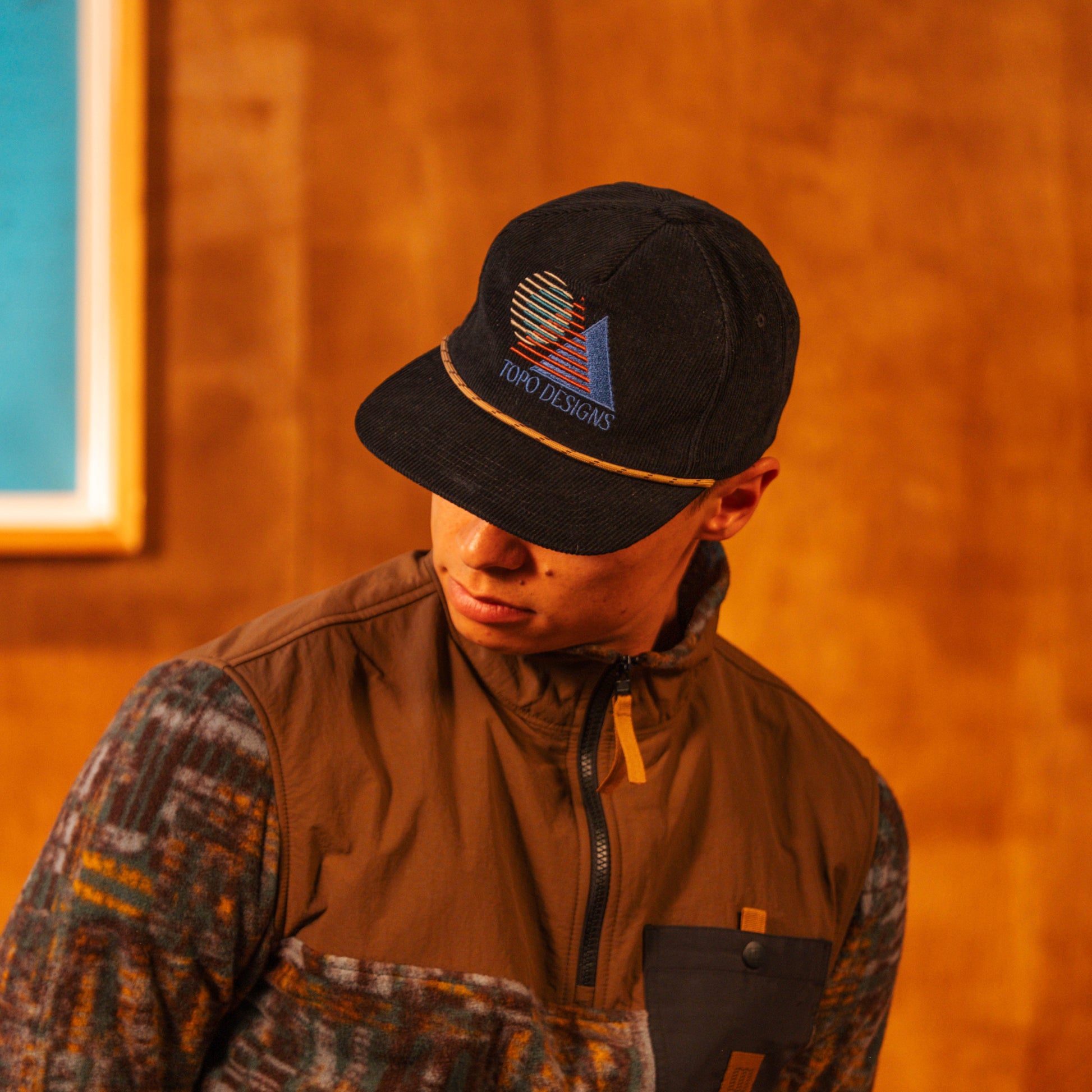 Person wearing a Corduroy Trucker Hat with a logo against an orange wall 