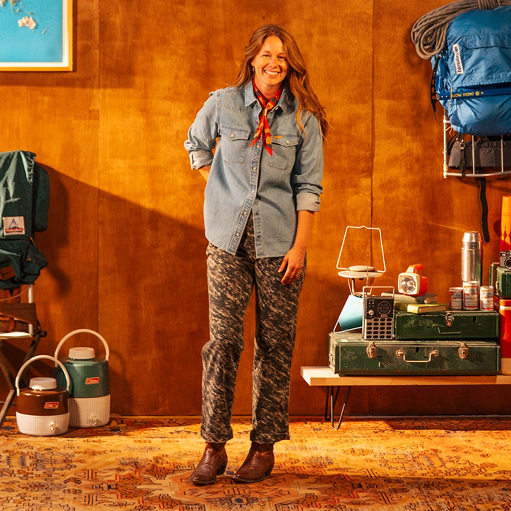 Woman wearing a denim shirt standing in front of a wooden wall with a map and equipment