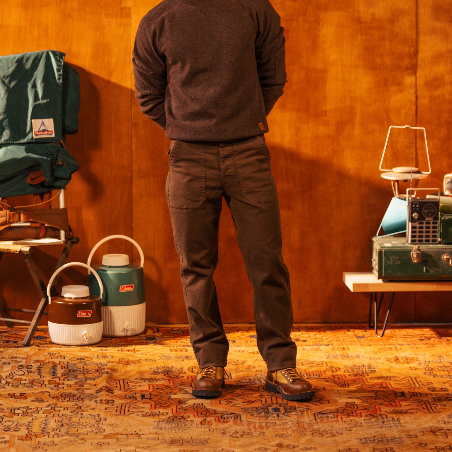 Person standing in a room with camping gear including a chair, coolers, and lanterns.