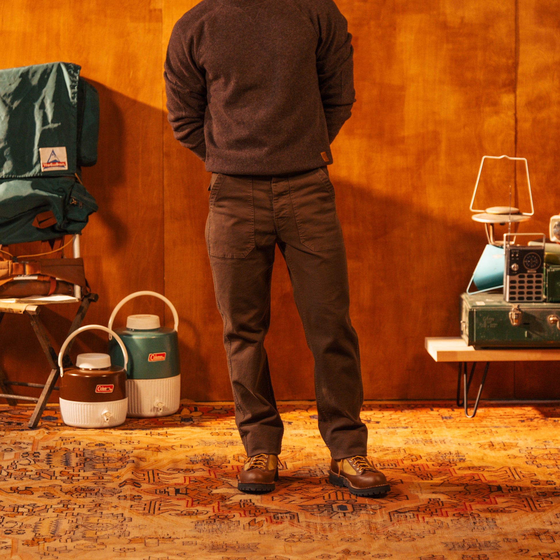 Person standing in a room with camping gear including a chair, coolers, and lanterns.