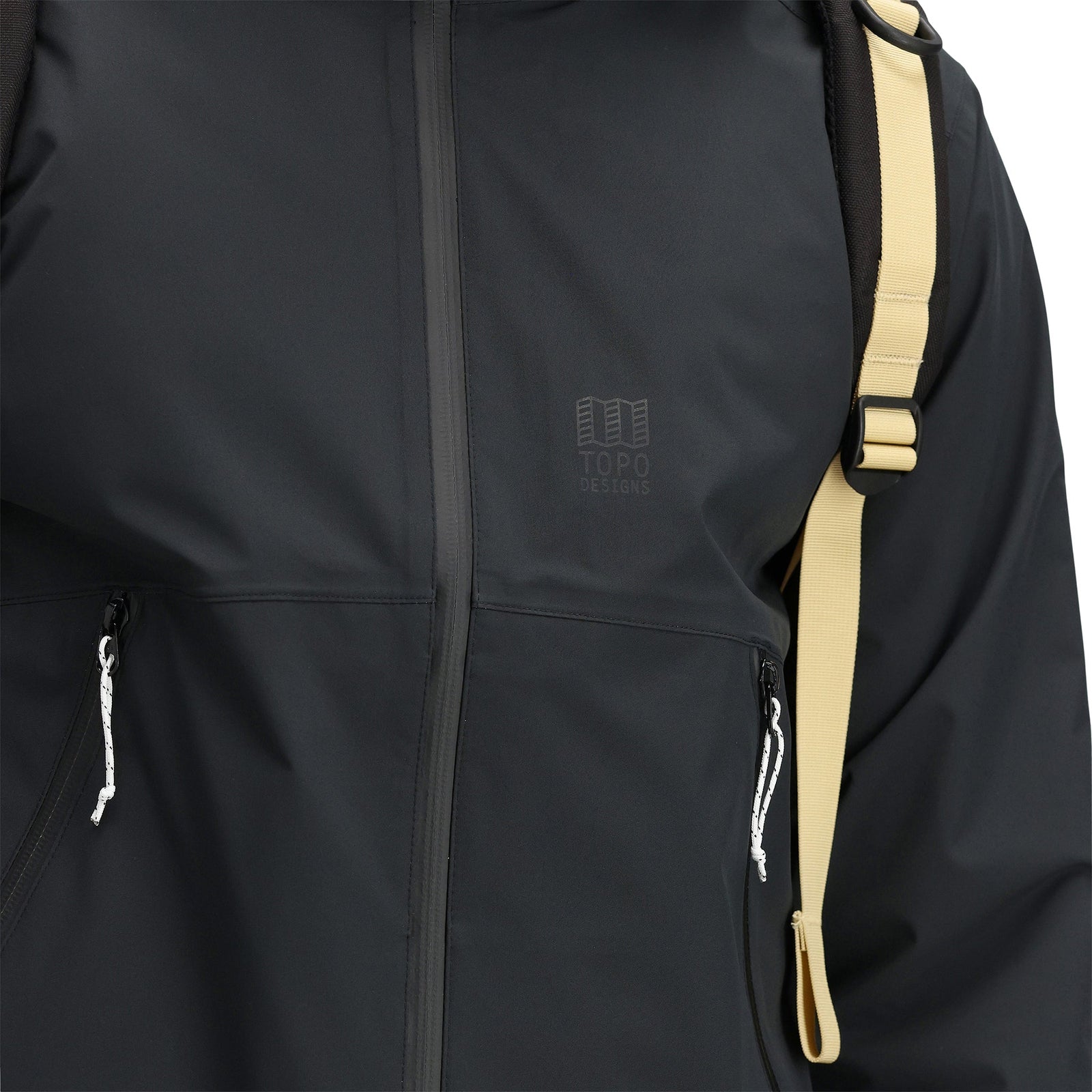 General detail shot of chest logo and zipper pulls on model wearing Topo Designs Men's Global Jacket packable 10k waterproof rain shell in recycled "black" polyester.