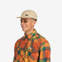 Side model shot of Topo Designs Nylon Camp 5-panel flat brim Hat in "Tan" brown.