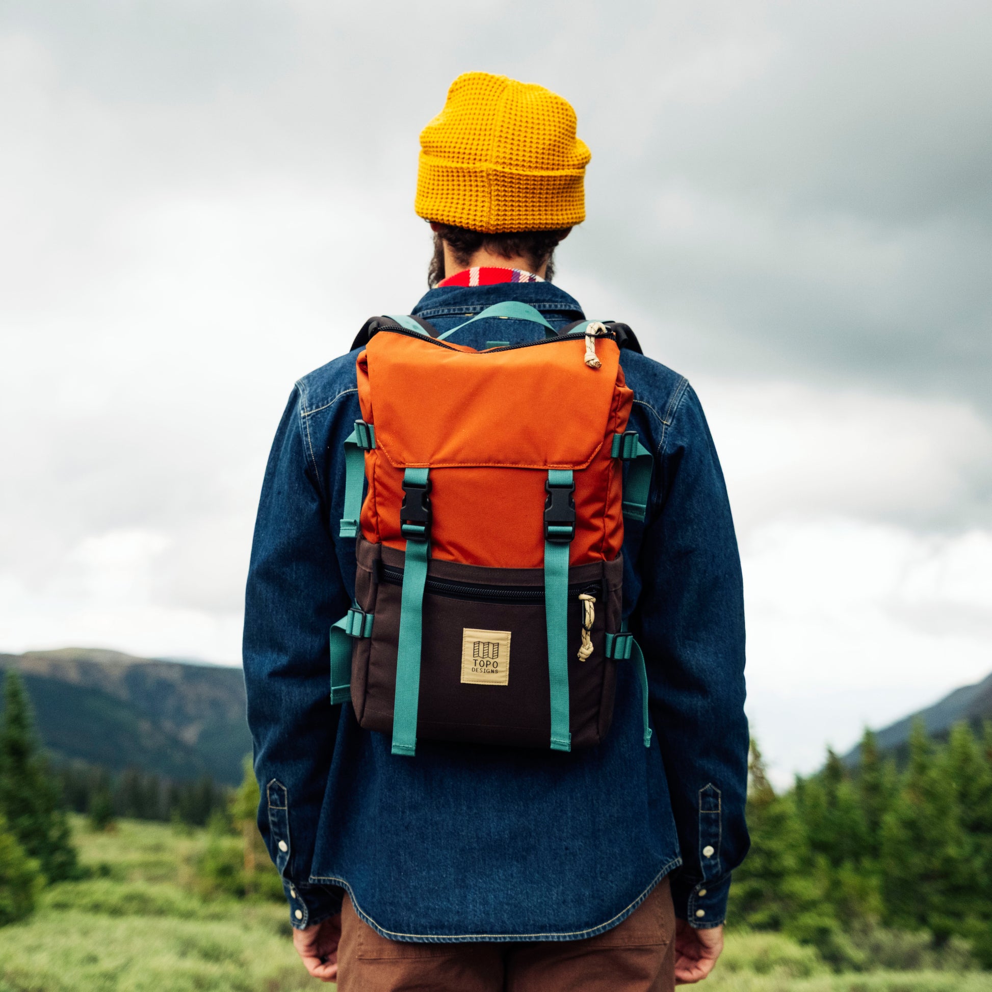 Person wearing a colorful backpack with mountains in the background