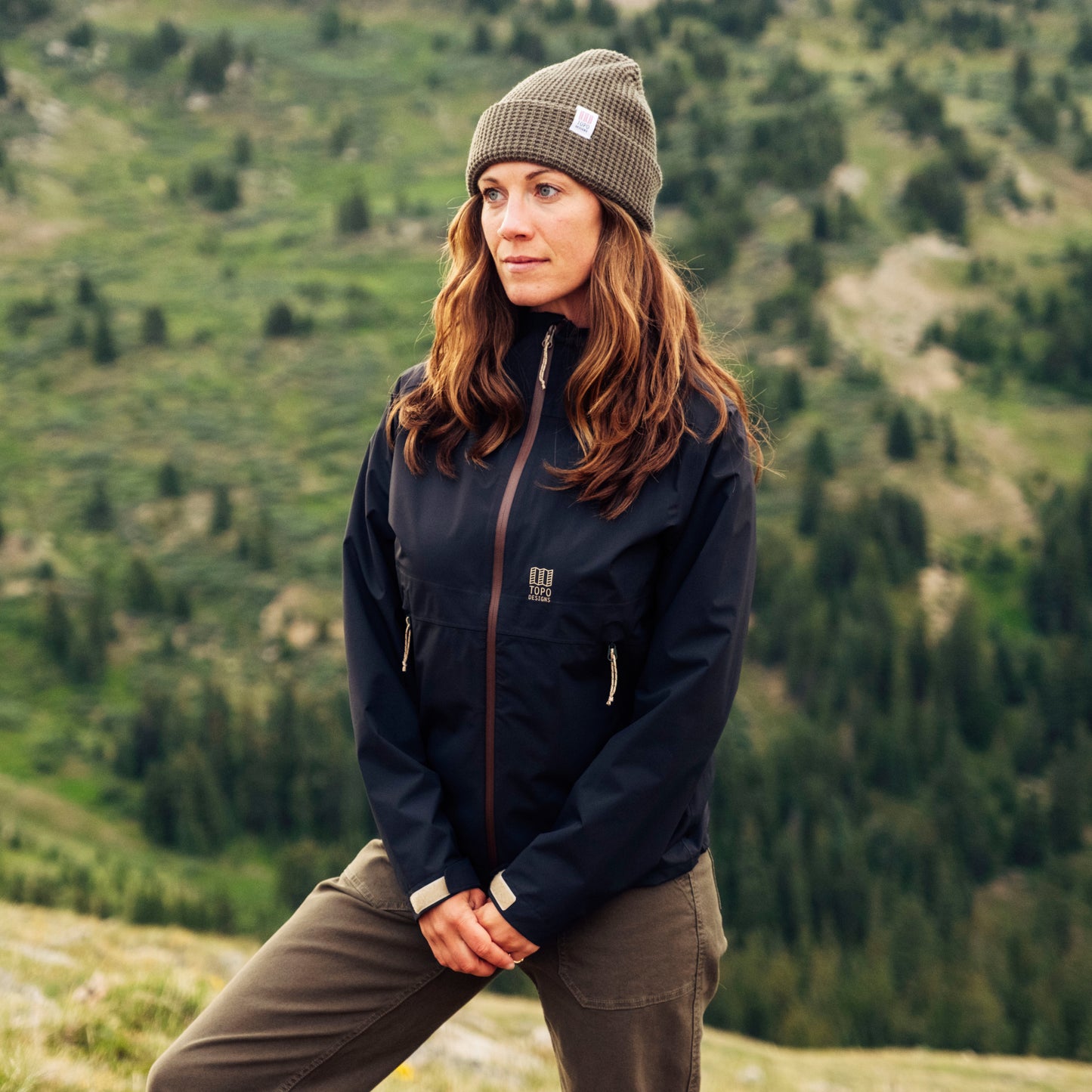 Person wearing a black jacket and gray beanie standing in a mountainous landscape