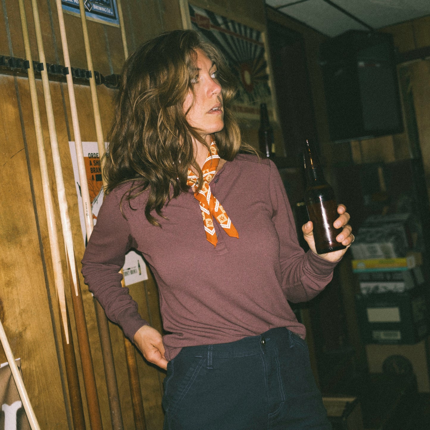 Person holding a bottle in a room with wooden walls and pool cues.