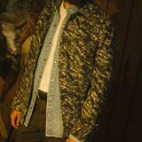 Person wearing a camouflage jacket over a denim shirt with a blurred background