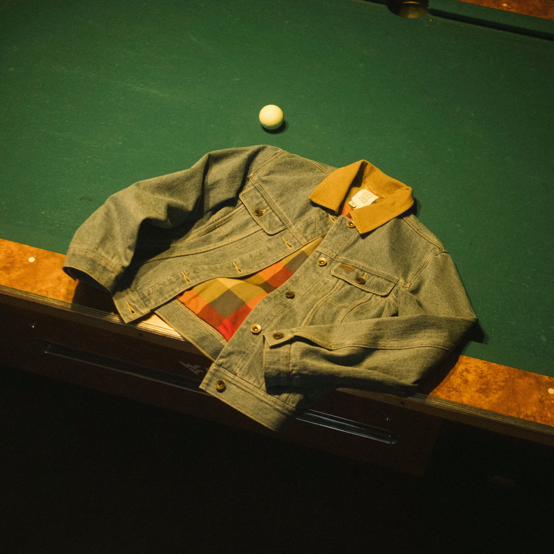 Green denim jacket on a pool table with a white ball
