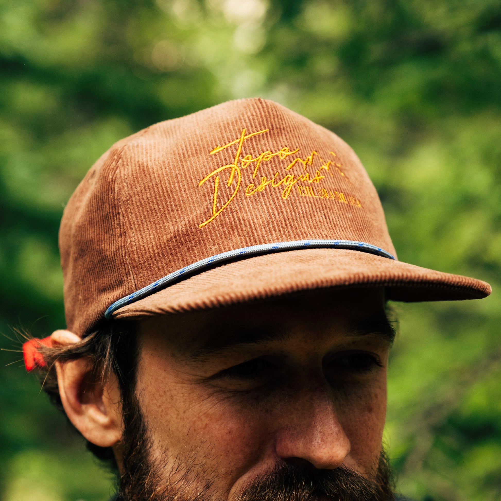 Brown cap with yellow text worn by a person with a blurred green background