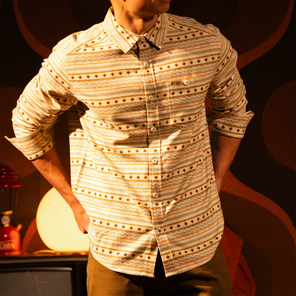 Person wearing a "Bone White Sunset Stripe" Mountain Shirt Lightweight with a dark background with a warm glow in a dimly lit room.