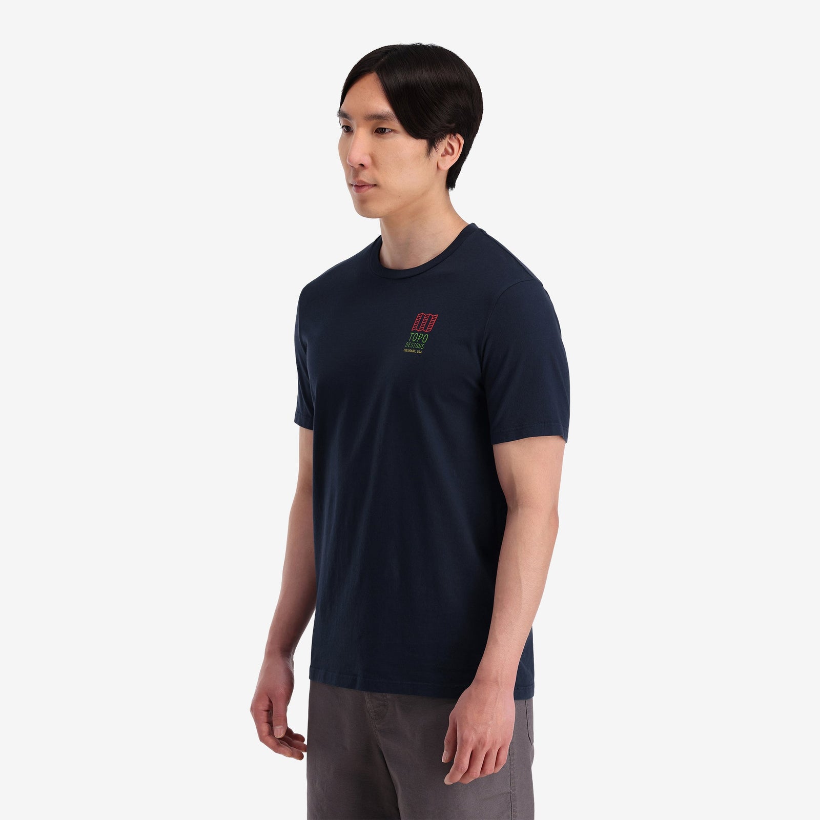 On model left side view of Topo Designs Men's Small Original Logo Tee 100% organic cotton short sleeve graphic logo t-shirt in "navy" blue.