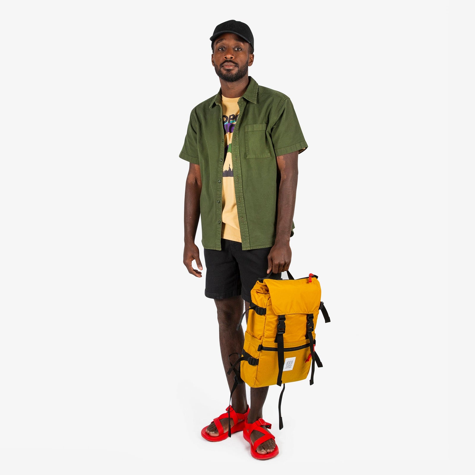 Topo Designs Rover Pack Classic in "Mustard" yellow held by model with top carry handle.