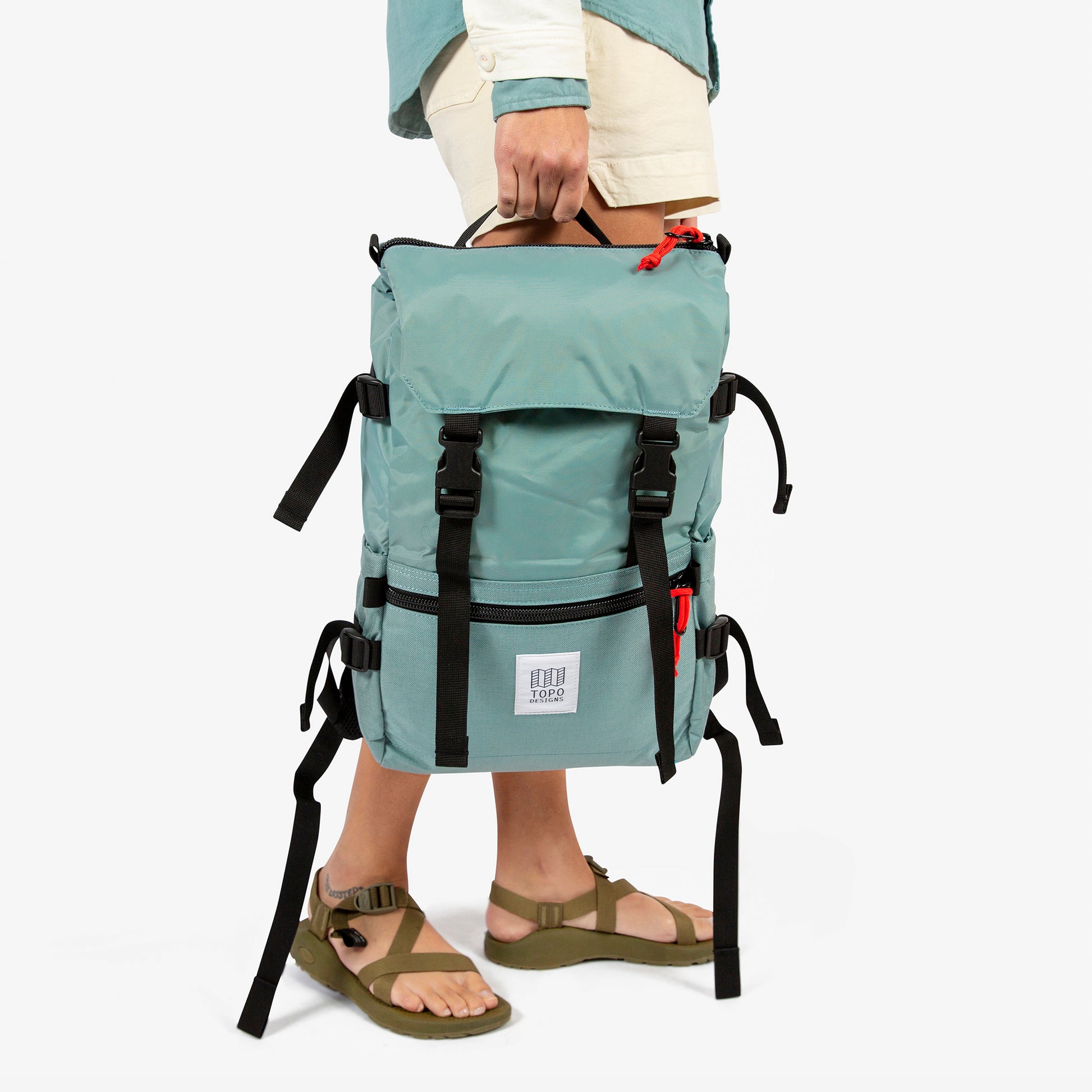 Topo Designs Rover Pack Classic in "Sage" green held by model with top carry handle.