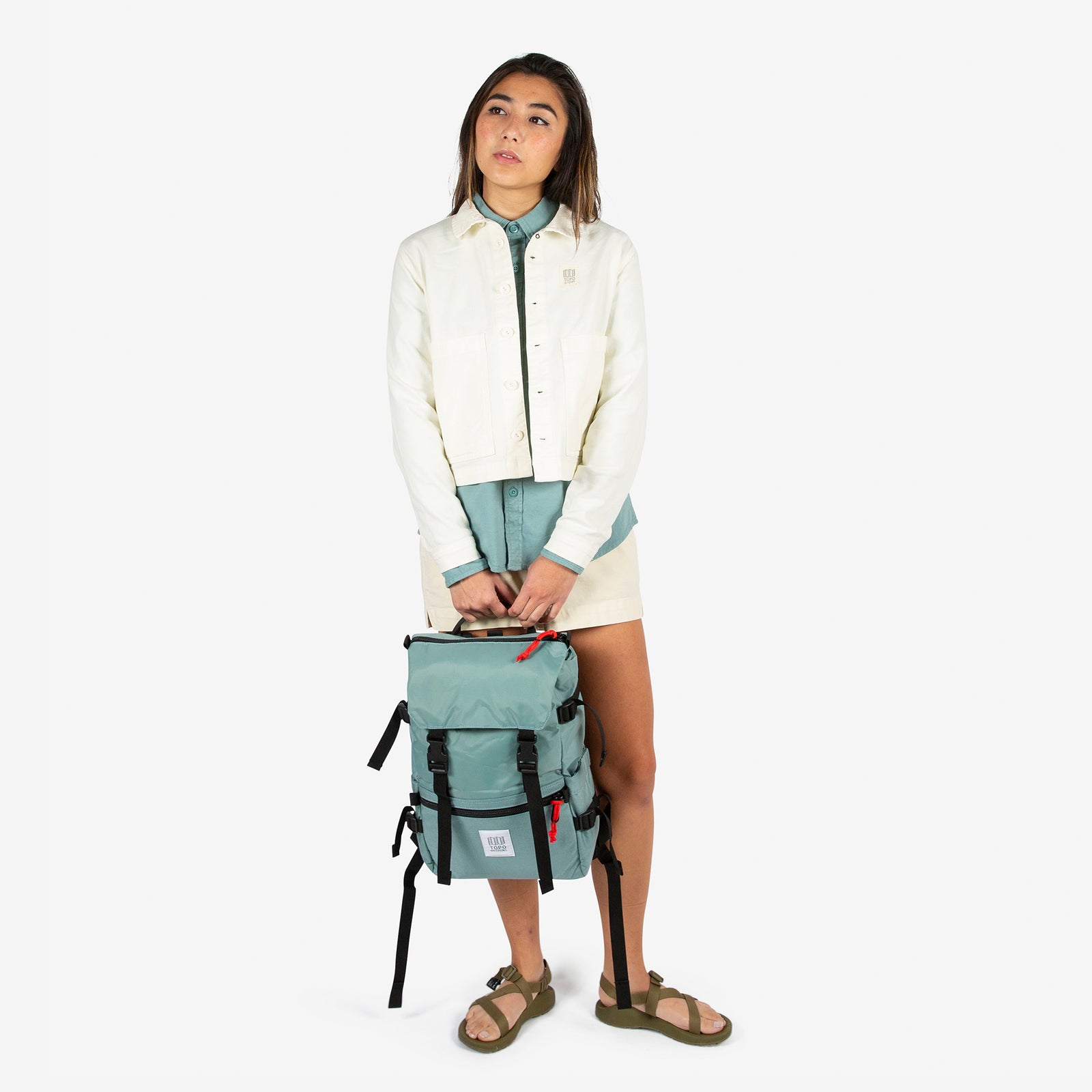 Topo Designs Rover Pack Classic in "Sage" green held by model with top carry handle.