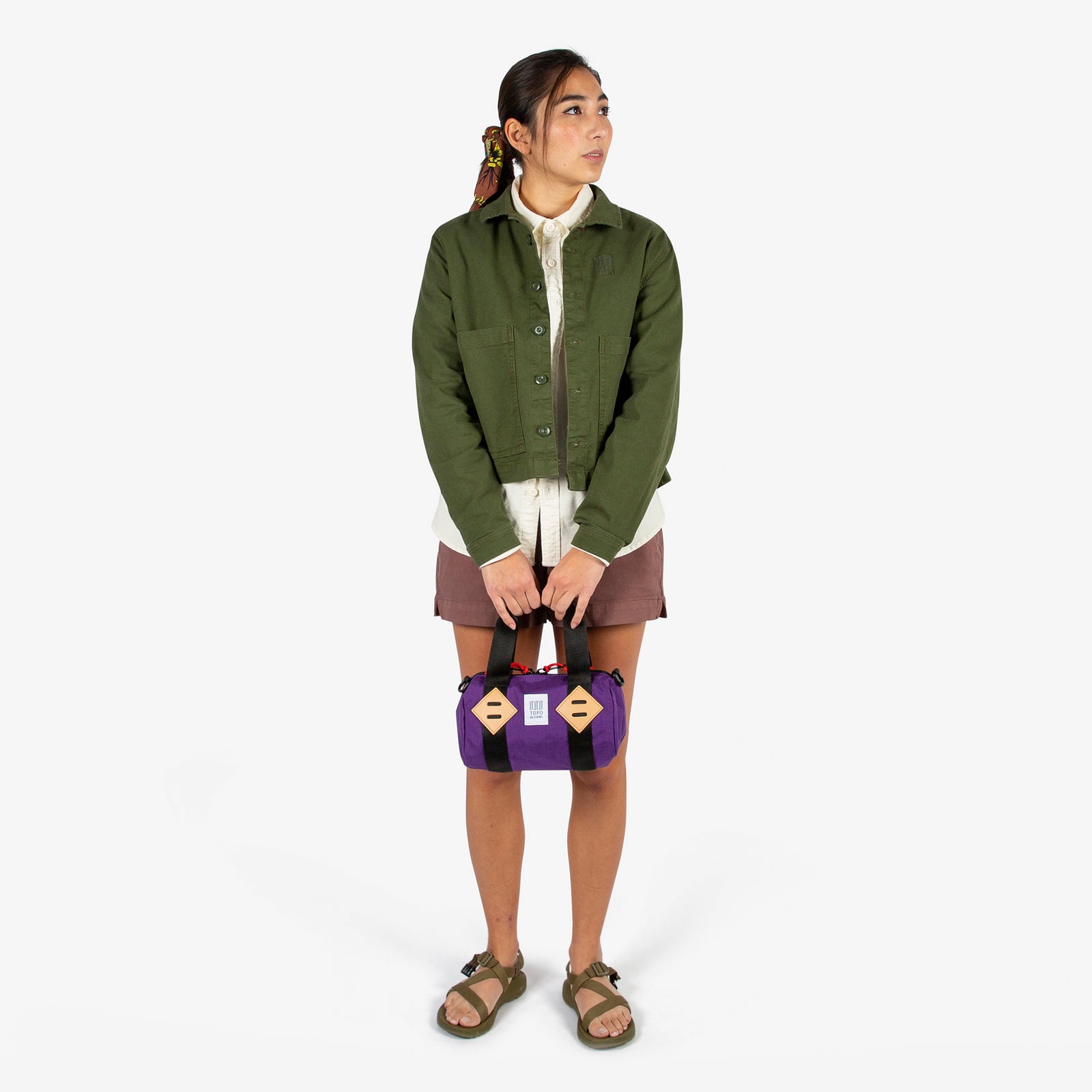 General shot of Topo Designs Mini Classic Duffel Bag shoulder crossbody purse in Purple held by model with top carry straps.