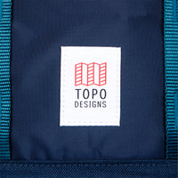 General shot of Topo Designs Global Travel Bag 30L Durable Carry On Convertible Laptop Travel Backpack in Navy blue showing close-up of front logo patch