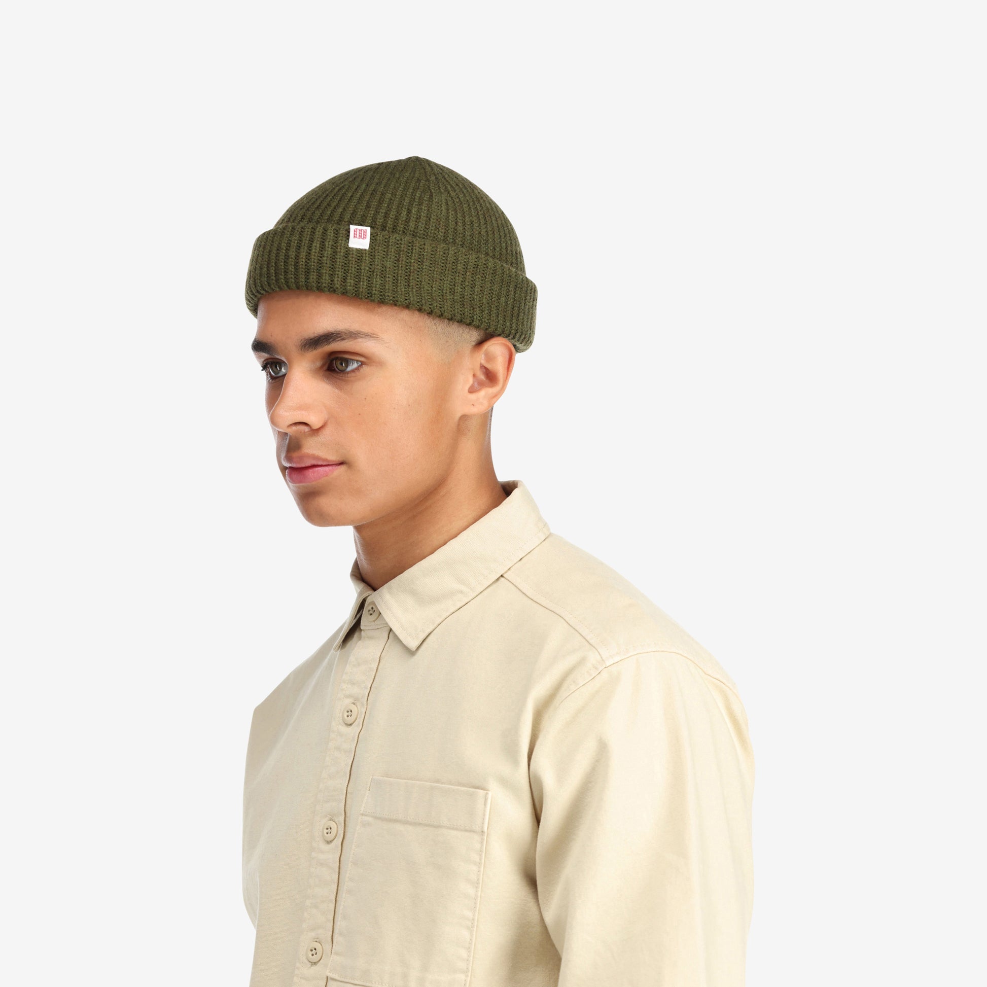 Side model shot of Topo Designs Global Beanie merino wool blend watchman cap in "olive" green.