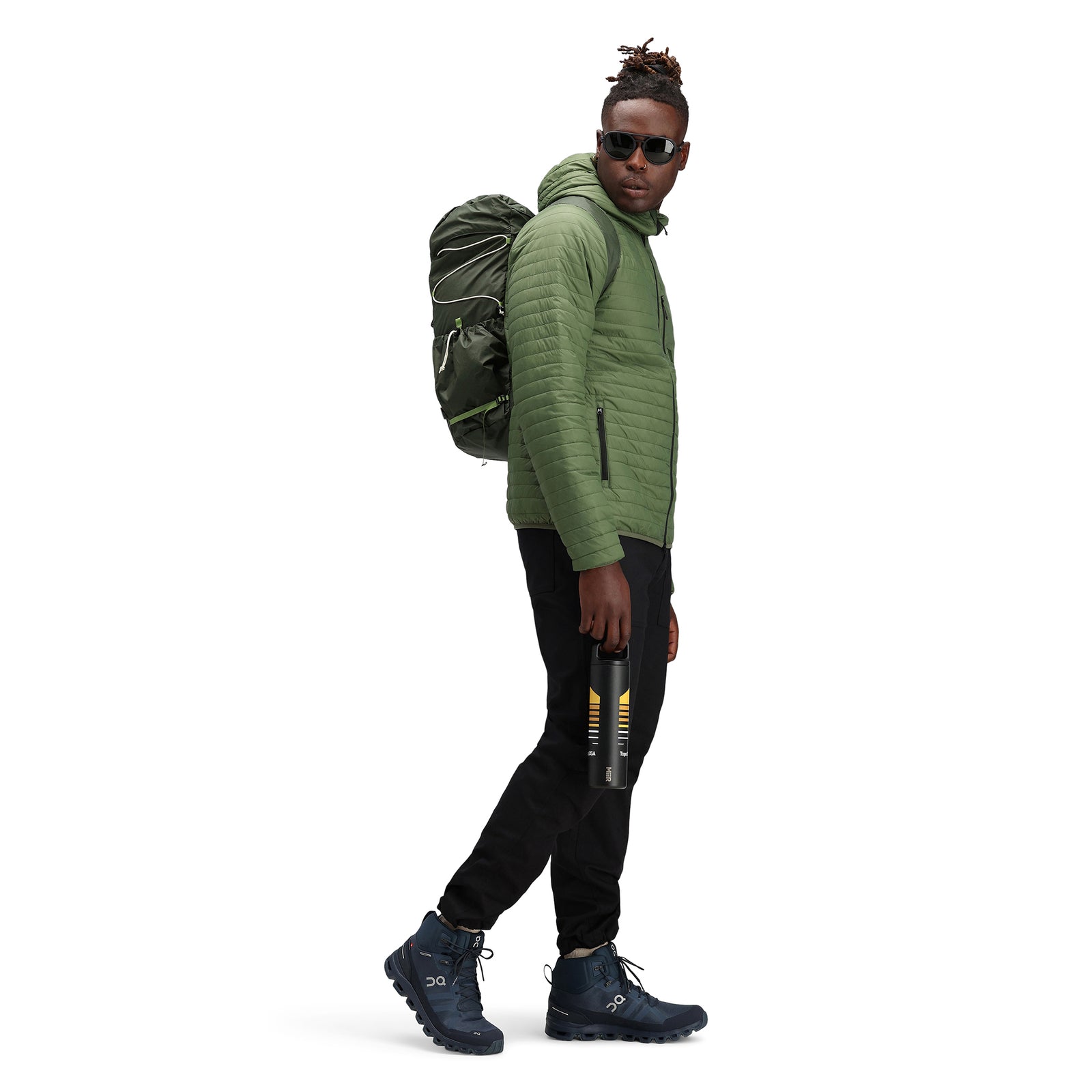 Model wearing Topo Designs Men's Global Puffer packable recycled insulated Hoodie jacket in "olive" green.