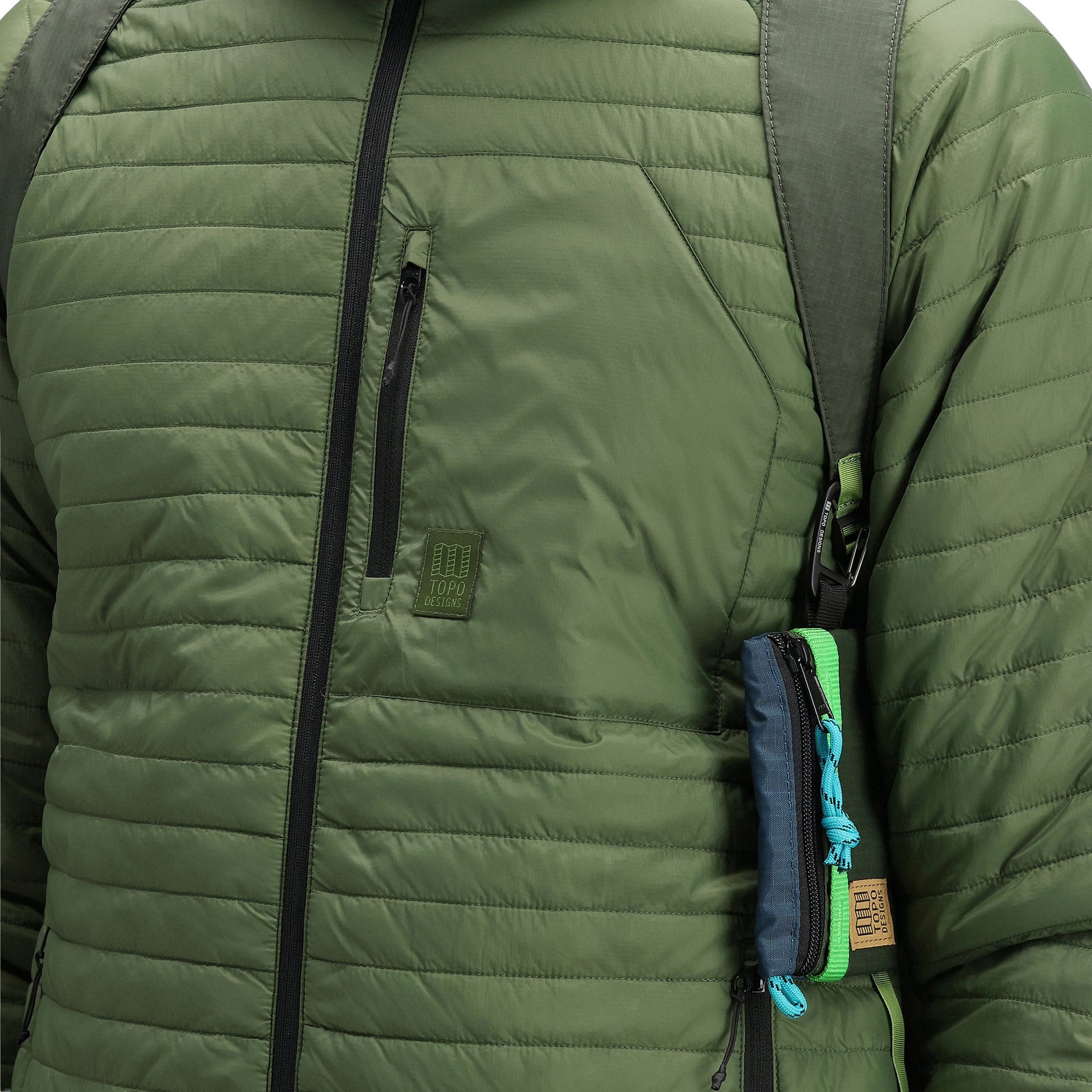 General detail shot of chest pocket and logo patch on model wearing Topo Designs Men's Global Puffer packable recycled insulated Hoodie jacket in "olive" green.