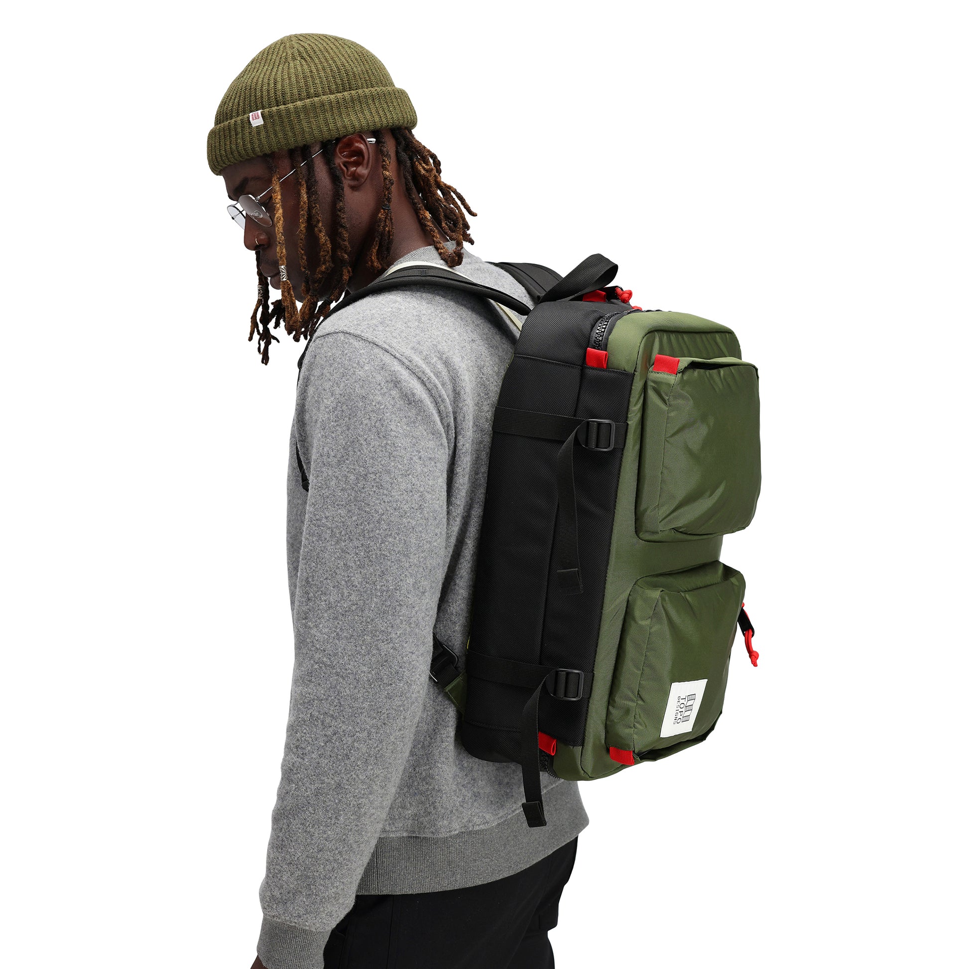 Model wearing Topo Designs Global Beanie merino wool blend watchman cap in "olive" green.