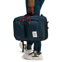 General front model shot showing  hand carry of Topo Designs Global Briefcase convertible laptop travel backpack in "Navy" blue nylon.