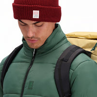 Front model shot showing zipper, collar, and logo patch on chest of Topo Designs Men's Puffer recycled insulated Jacket in "forest" green
