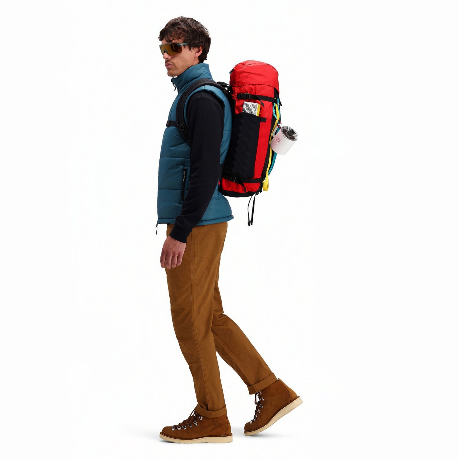 Model wearing Topo Designs Mountain Pack 28L hiking backpack with external laptop sleeve access in lightweight recycled "Red / Turquoise" nylon.