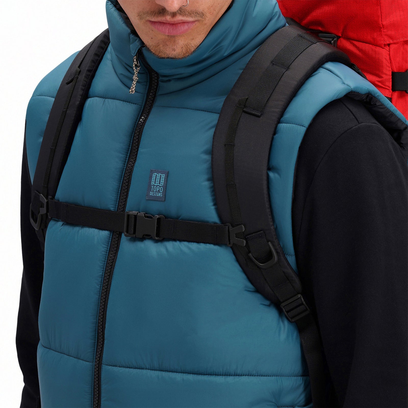 General shot of model wearing sternum strap on Topo Designs Mountain Pack 28L hiking backpack with external laptop sleeve access in lightweight recycled "Red / Turquoise" nylon.