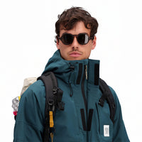General front model shot showing velcro and zipper on Topo Designs Men's Mountain Parka waterproof shell jacket in "Pond Blue"