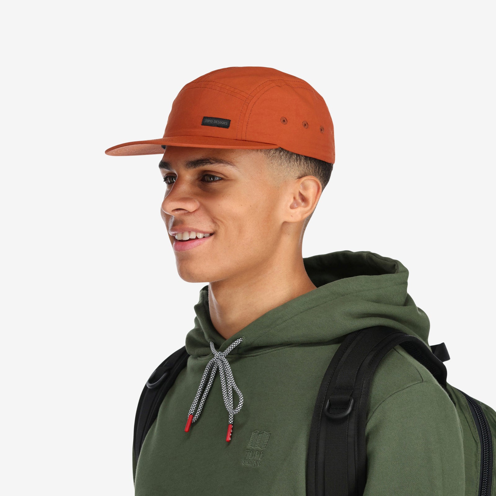 General side model shot of Topo Designs Nylon Camp 5-panel flat brim Hat in "brick" orange