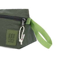 General detail shot of handle, logo patch, and zipper pull on Topo Designs TopoLite Dopp Kit ultralight toiletry bag for travel in "olive" green.