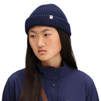 Model wearing Topo Designs Global Beanie merino wool blend watchman cap in "navy" blue.