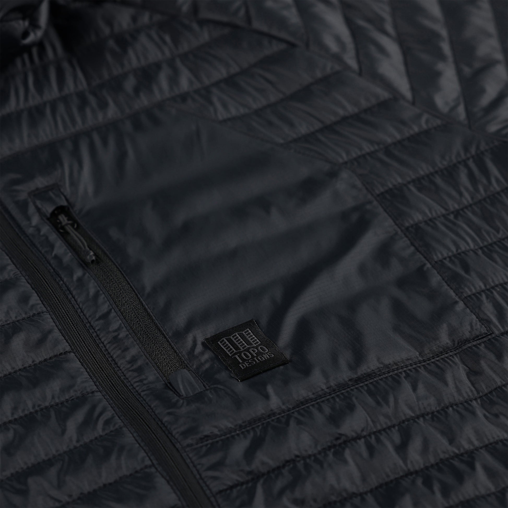 General detail shot of zipper chest pocket on Topo Designs Women's Global Puffer recycled insulated packable Hoodie jacket in "black"