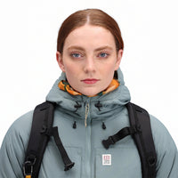 General front model shot of Topo Designs Women's Puffer Primaloft insulated Hoodie jacket in "slate" blue showing hood cinch cords.