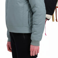 General side model shot of Topo Designs Women's Puffer Primaloft insulated Hoodie jacket in "slate" blue showing hand pocket and cuff.