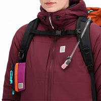 General front model shot of Topo Designs Women's Puffer Primaloft insulated Hoodie jacket in "burgundy" red showing chest zipper pockets and  logo.