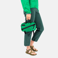 General side model shot of Topo Designs Mini Quick Pack in green showing handheld carry.