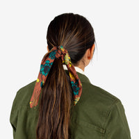 General shot of Topo Designs bandana in brick green Tour floral print tied around model's pony tail.