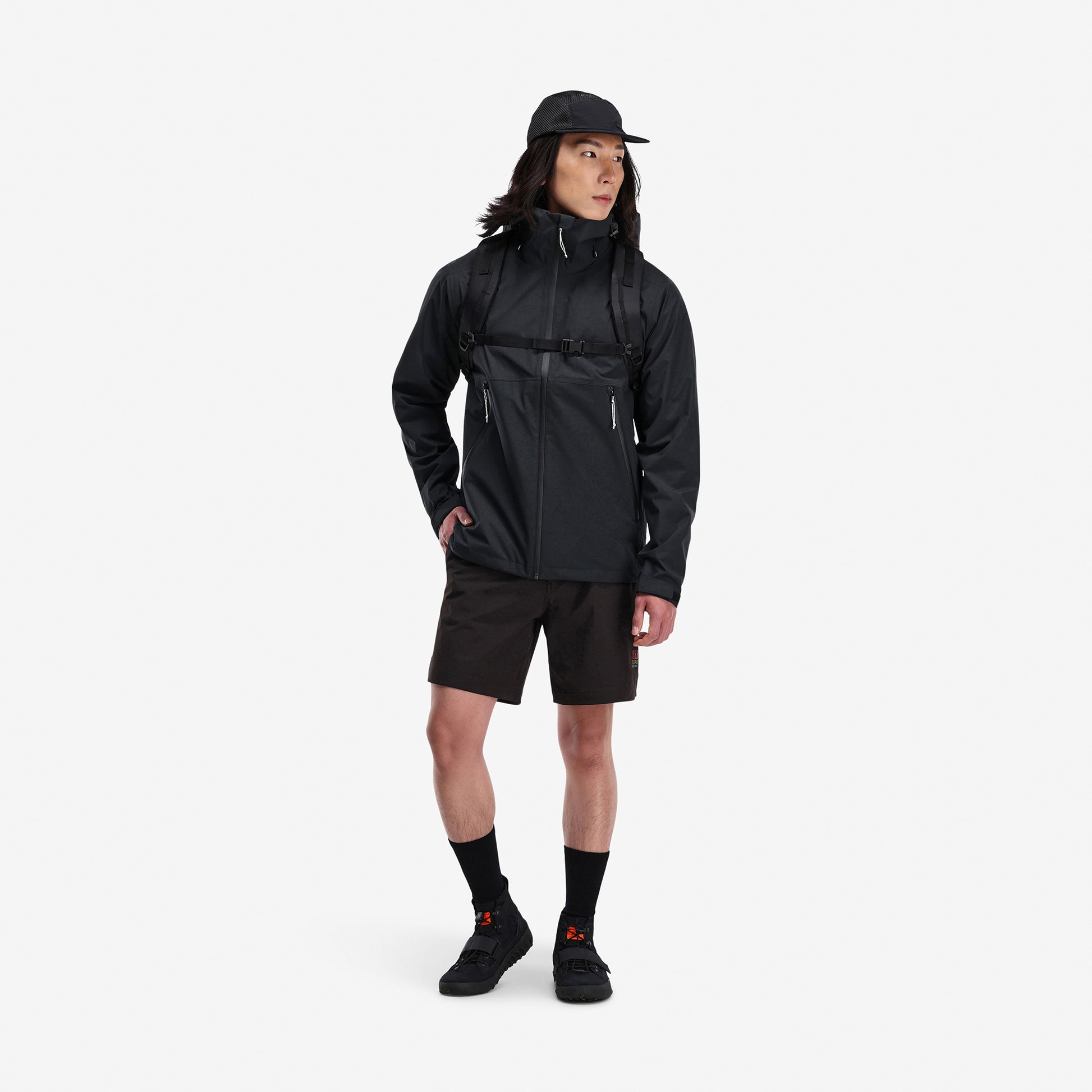 Model wearing Topo Designs Men's Global Jacket packable 10k waterproof rain shell in recycled "black" polyester.