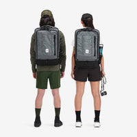 Models wearing Topo Designs Global Travel Bag 40L Durable Carry On Convertible Laptop Travel Backpack in Charcoal gray.