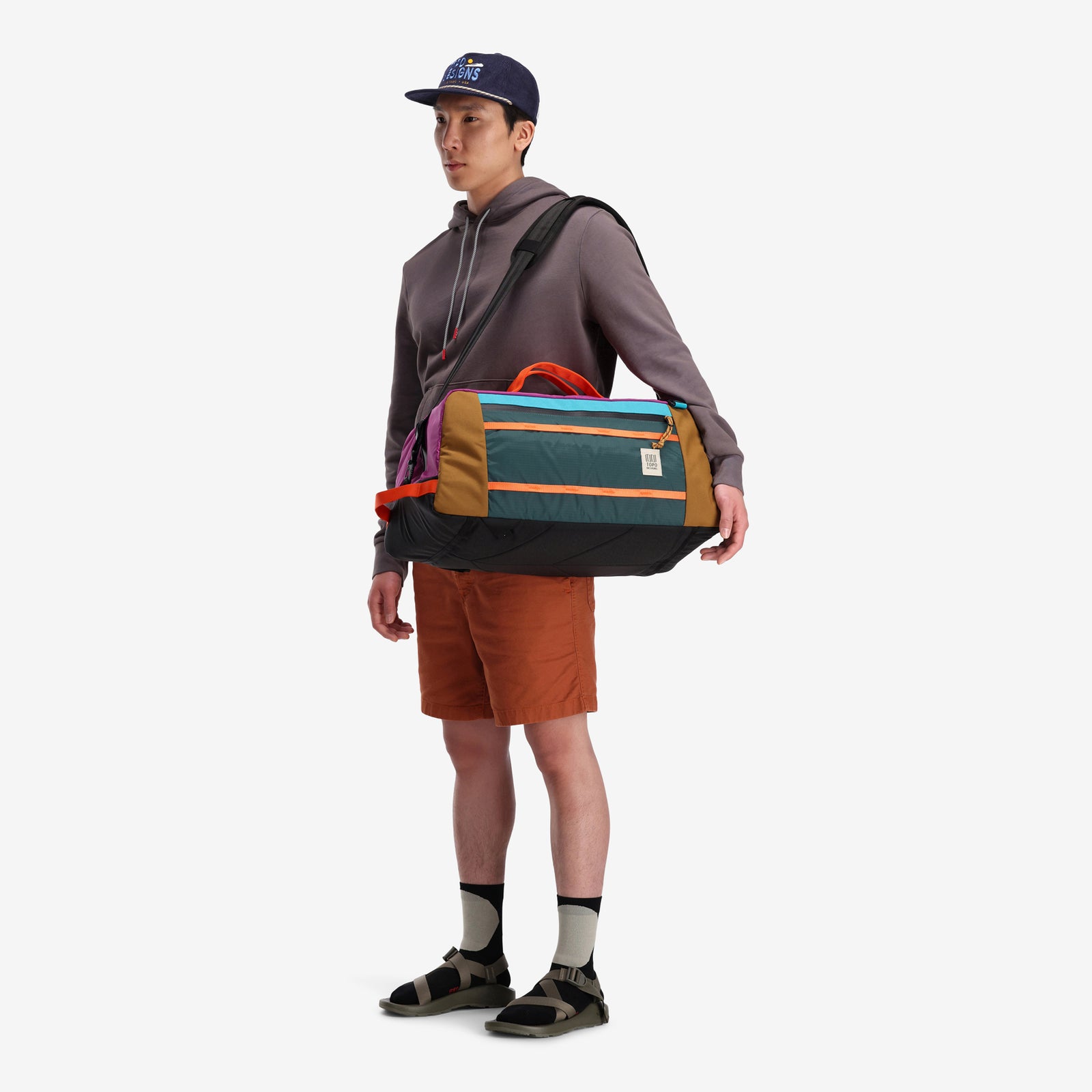 General shot of model wearing Topo Designs Mountain Duffel 40L backpack gear bag in recycled "Botanic Green / Grape" nylon.